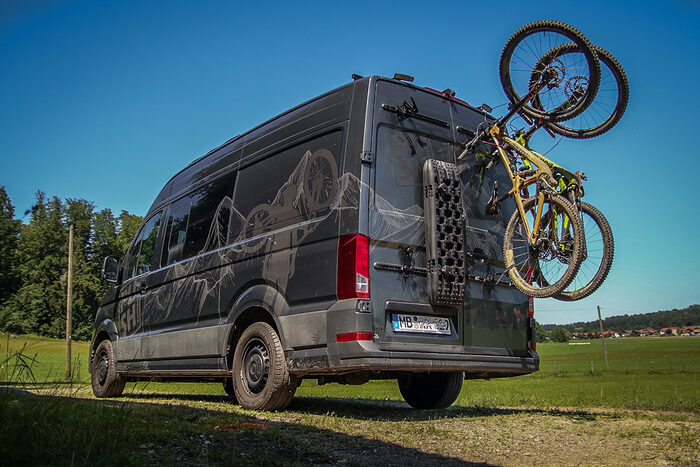 This picture shows a camper with vertical PUSHrack rear carriers. Two mountain bikes and a sand tray are mounted on it. The products are from PUSH components.