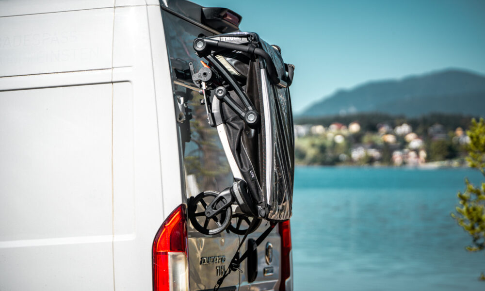 Zusammengefalteter Kinderfahrradanhänger am PUSHrack am Heck eines Campervans befestigt