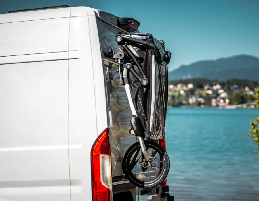 Zusammengefalteter Kinderfahrradanhänger am PUSHrack am Heck eines Campervans befestigt