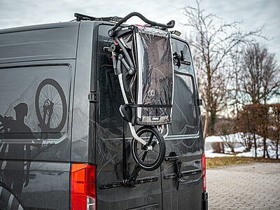 Gefalteter Kinderfahrradanhänger am PUSHrack am Heck eines Campervans befestigt
