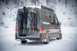 Campervan mit PUSHrack Ski- und Snowboardträger, auf dem mehrere Paar Ski und ein Snowboard sowohl mit als auch ohne Tasche sicher am Heck befestigt sind in verschneiter Winterlandschaft