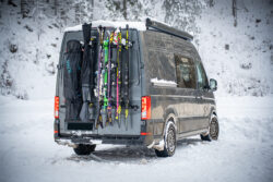 Campervan mit PUSHrack Ski- und Snowboardträger, auf dem mehrere Paar Ski und ein Snowboard sowohl mit als auch ohne Tasche sicher am Heck befestigt sind in verschneiter Winterlandschaft