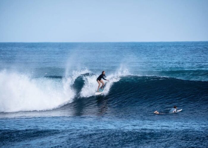 Zu sehen ist eine Frau die mit ihrem Surfbrett eine Wellt reitet