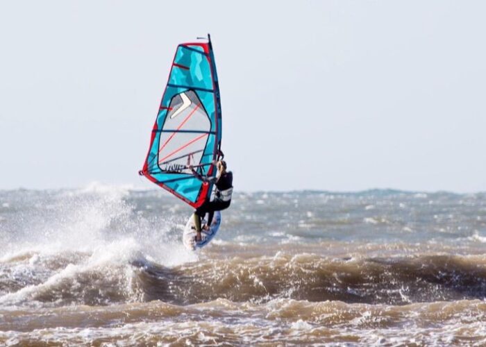 Zu sehen ist eine Windsurferin die gerade über eine Welle springt